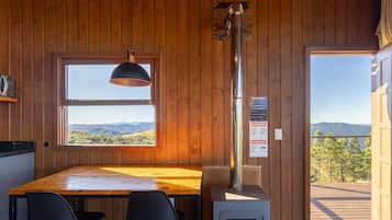 Un interno in legno con un tavolo da pranzo, sedie, una lampada a sospensione e vista sulle montagne attraverso una finestra.
