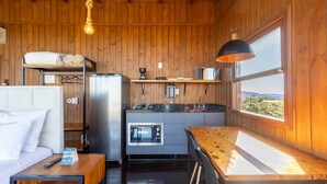 A compact kitchen with a refrigerator, oven, and coffee maker, wooden walls, and a window with a view. - Cabana com Vista Incrível VST001 (Anitapolis)