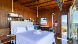 A wooden cabin with a bed, a table, chairs, and a view of the mountains. - Cabana com Vista Incrível VST001 (Anitapolis)