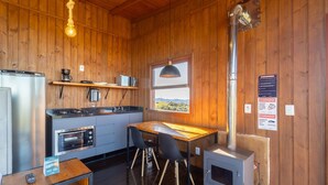 Cocina compacta con paredes de madera, estufa a gas, horno integrado, máquina de café y ventana con vistas al exterior.
