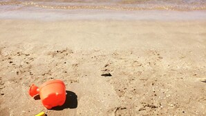 Una spiaggia con una singola bottiglia arancione sulla sabbia, vicino al mare.