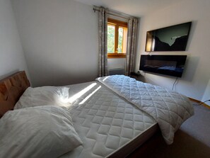 A bedroom with a bed, a window with curtains, a wall-mounted TV, and a radiator.