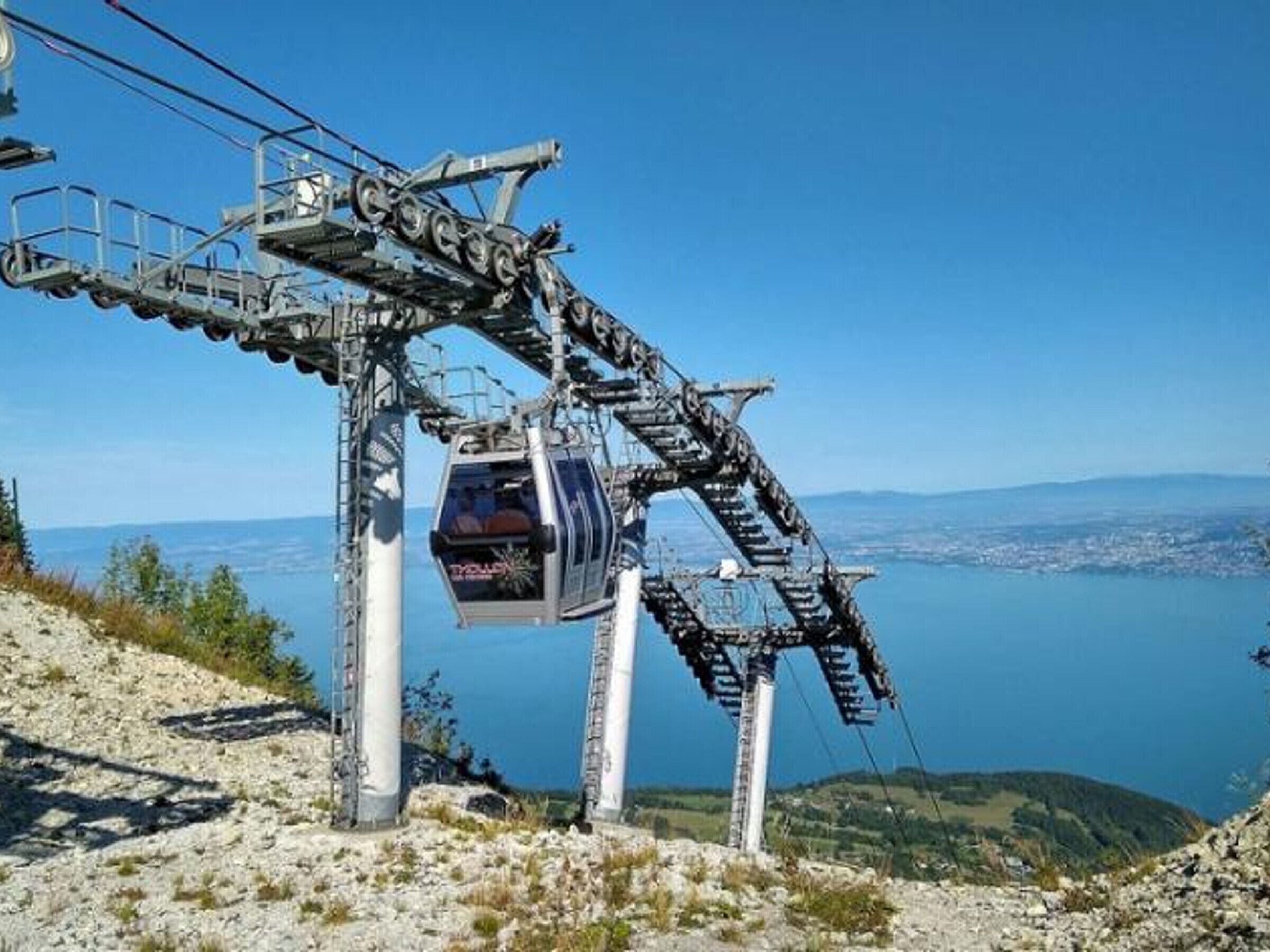 A cable car system with a gondola at the station, overlooking a body of water and distant landscape.