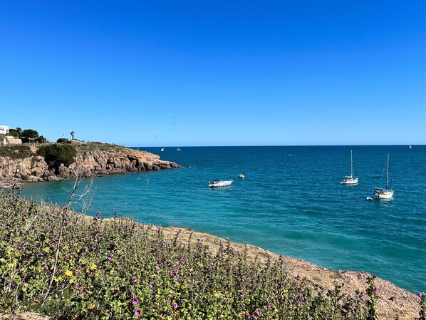 A coastal scene with rocky cliffs, clear blue sea, and boats.