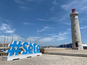 A lighthouse and a large '#Sète' sign in front of it.