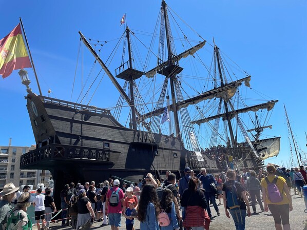 A large crowd of people gathered around a historic ship with multiple masts and rigging.
