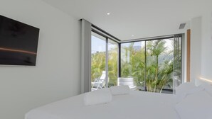A modern bedroom with a large bed, a TV mounted on the wall, and a balcony with a chair and plants. - Casa Miravella (Adeje)