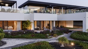 A modern multi-story building with glass balconies, outdoor seating, and a landscaped garden. - Casa Miravella (Adeje)