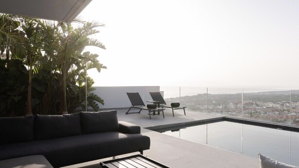 Un moderno espacio lounge al aire libre con una piscina infinita de cristal, un sofá y dos sillones de relax.