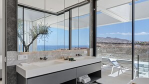 A modern bathroom with two sinks, a large mirror, and a view of the landscape.