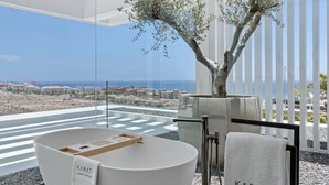 A modern bathroom with a bathtub, a tree, and a view of the beach and city.