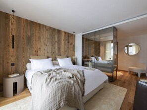 Een moderne slaapkamer met een houten wand, een groot bed met witte beddengoed, een nachtkastje, een spiegel en een klein zithoekje.