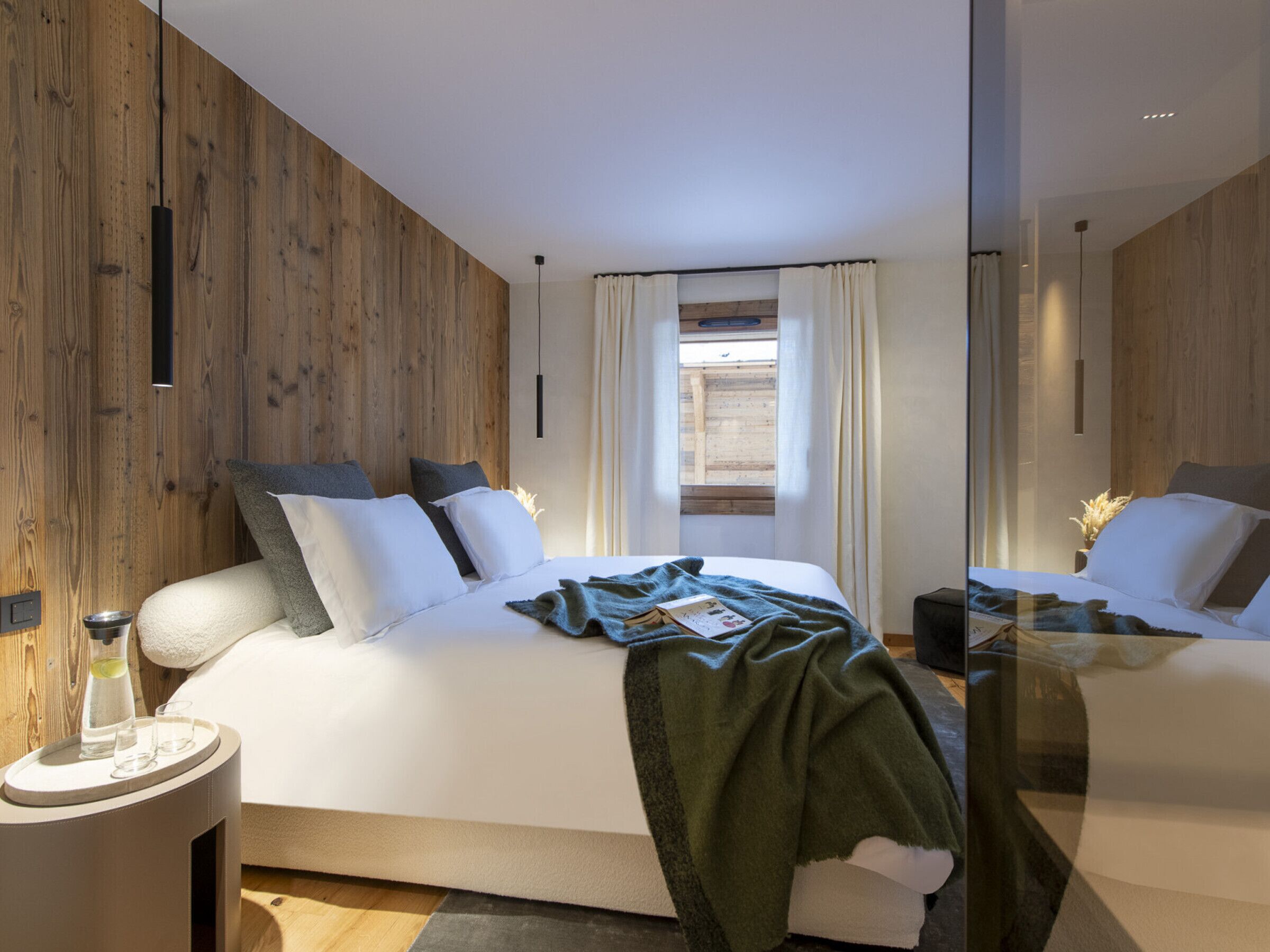 Une chambre moderne avec un mur en bois, un grand lit avec une literie blanche, une table de chevet avec une bouteille et des verres, et une fenêtre avec des rideaux.
