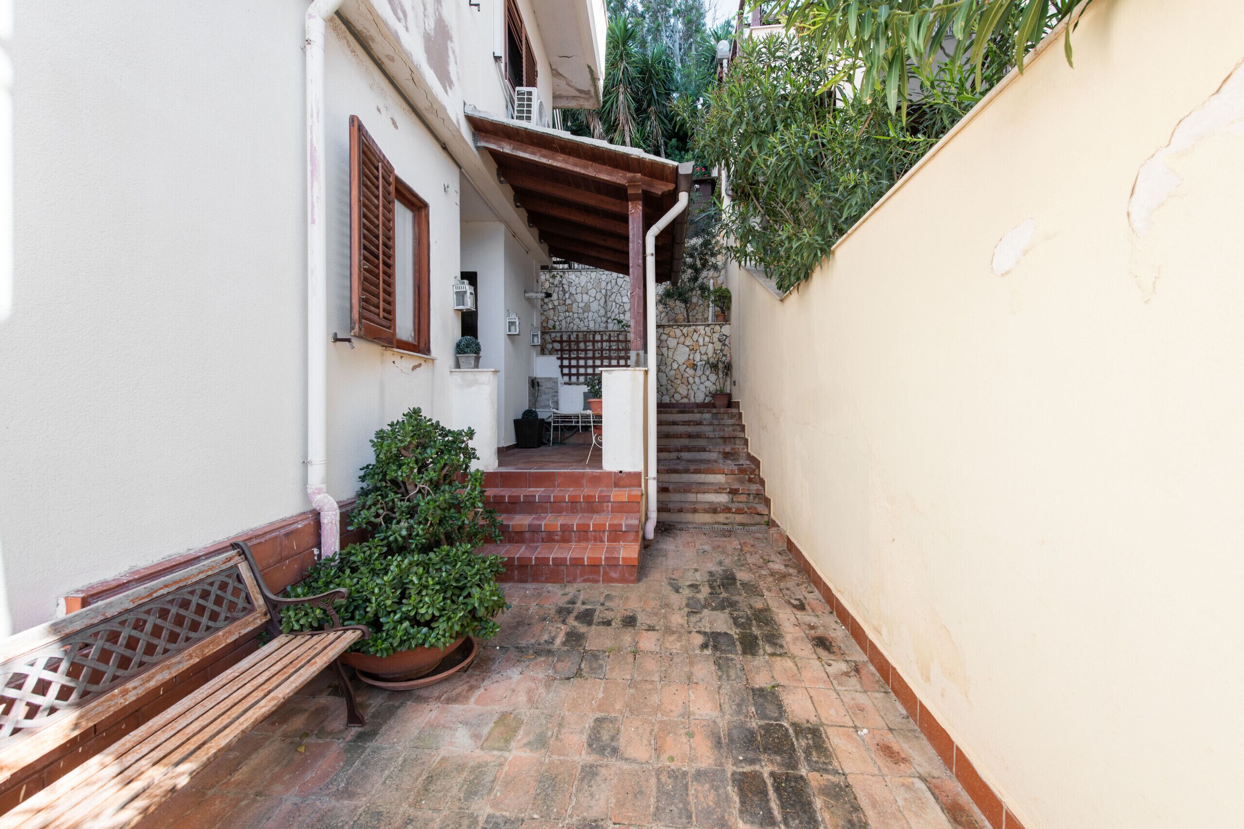 Une ruelle étroite avec un banc en bois, des plantes en pot et un escalier menant à l’entrée d’un immeuble.