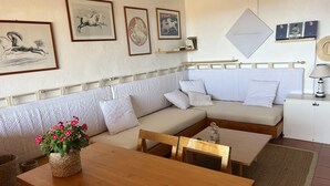 Ein modernes Wohnzimmer mit einem Ecksofa, einem Holztisch und einem Esstisch. An der Wand hängen gerahmte Gemälde von Pferden und auf dem Nachttisch steht eine Lampe.