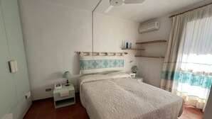 Ein Schlafzimmer mit einem Bett, einem Nachttisch, einer Lampe, einem Deckenventilator und einem Fenster mit Vorhängen.