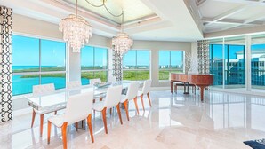 A spacious dining area with a piano, large windows offering a view of the ocean, and a chandelier.