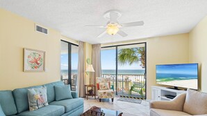 Ein Wohnzimmer mit Sofa, Sessel und Fernseher mit Blick auf einen Strand.