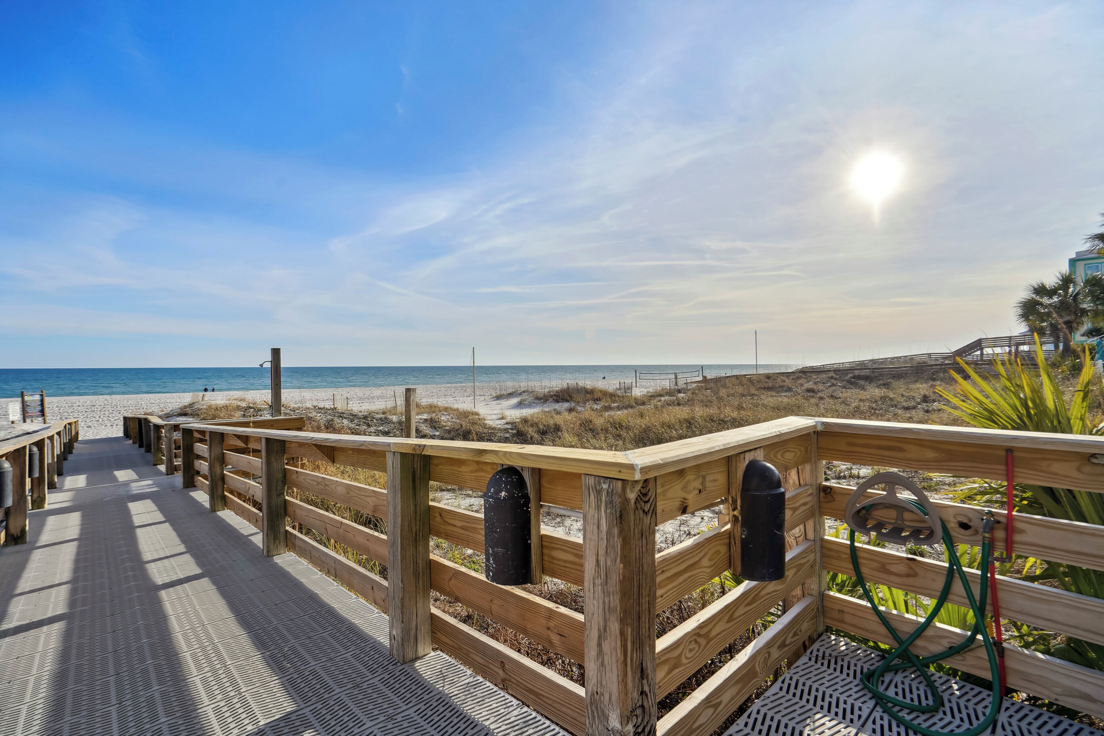 A wooden boardwalk leading to a beach with a clear sky and sun.