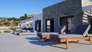 A modern outdoor lounge area with wooden loungers and a stone wall backdrop.