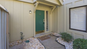 Una casa con puerta verde, un cartel con el número 721 y un pequeño jardín con piedras y plantas.