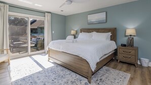 Un dormitorio con cama, mesita de noche, ventilador de techo, ventana con cortinas y vistas al exterior.