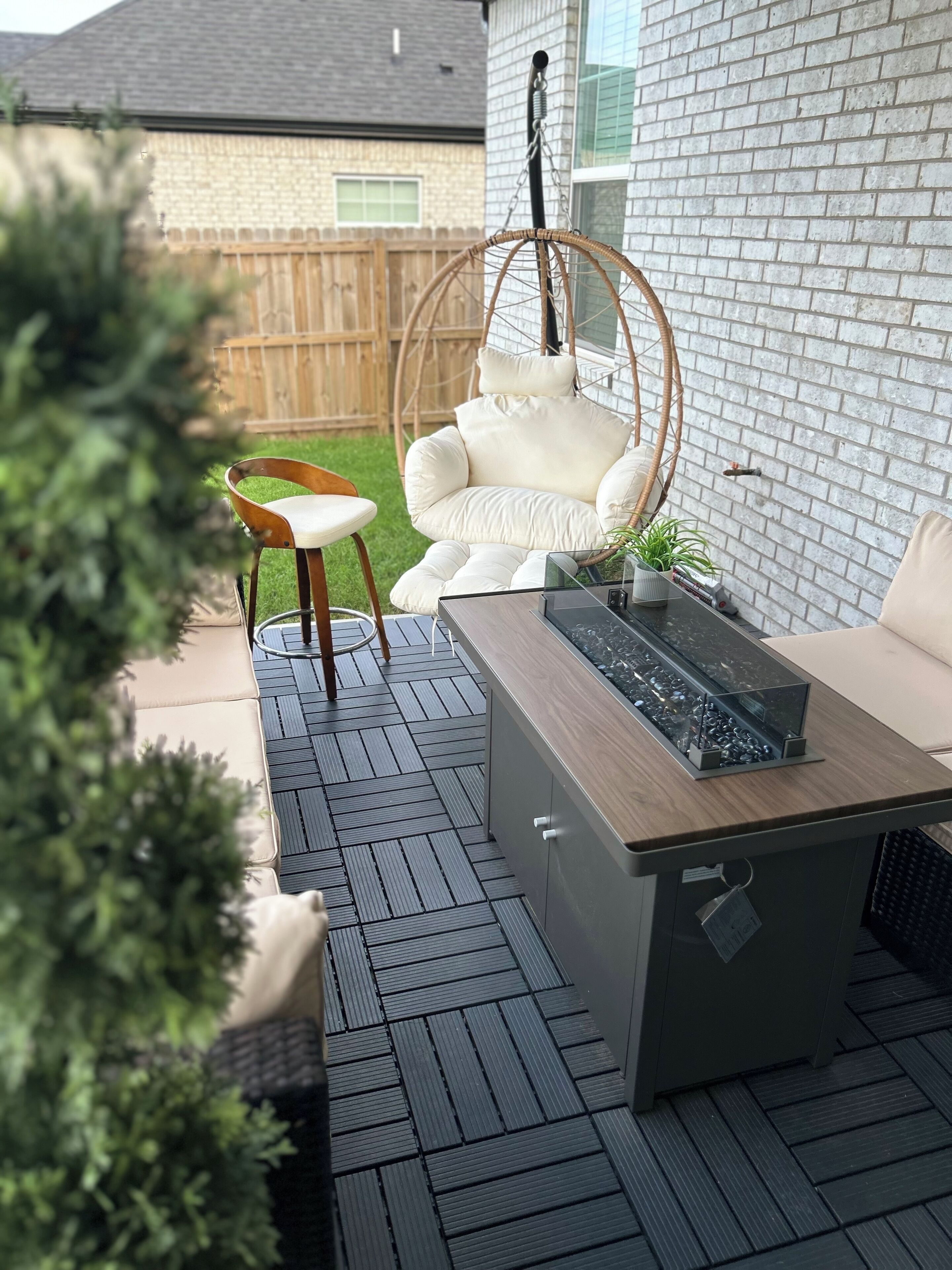 A deck with a wooden table, a hanging chair, and a small fire feature.