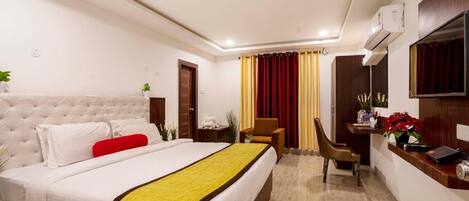 Quarto de hotel com cama, escrivaninha, cadeira e televisão fixada na parede.