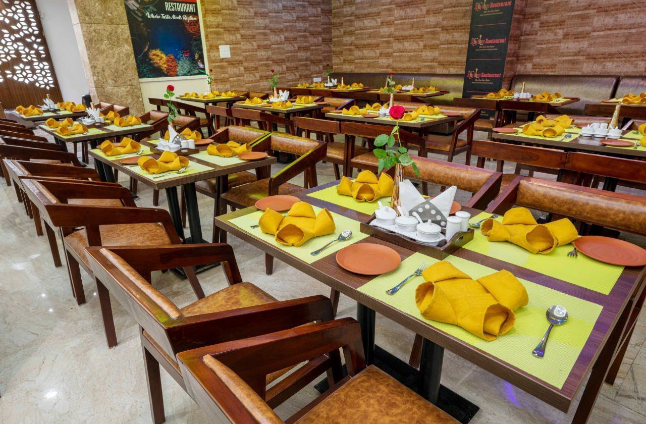 A restaurant with multiple tables set with yellow napkins, plates, and cutlery.