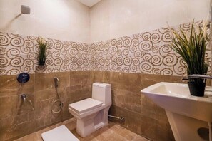 A bathroom with a toilet, bidet, and sink, surrounded by patterned tiles and potted plants.