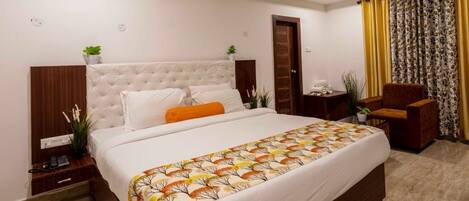 Habitación de hotel con una cama grande, una mesita de noche con teléfono, una silla y una ventana con cortinas.
