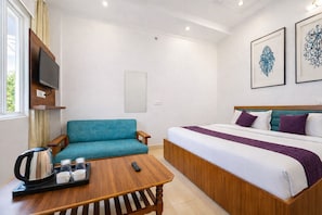 A hotel room with a bed, a sofa, a coffee table, and a TV. - Murli Manohar Palace (Vrindavan)