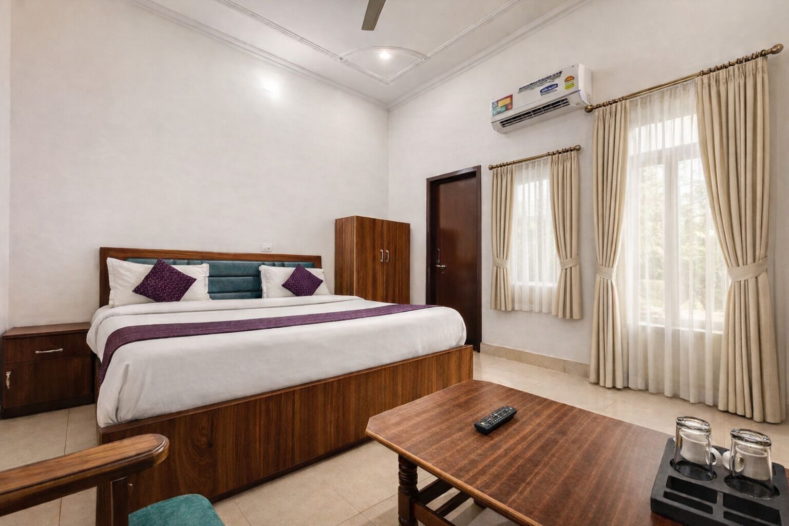Une chambre d’hôtel avec un lit, une table de chevet en bois, un bureau avec une télécommande et une fenêtre avec des rideaux.