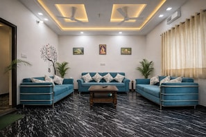A modern living room with two blue sofas, a wooden coffee table, and a ceiling fan. - Murli Manohar Palace (Vrindavan)