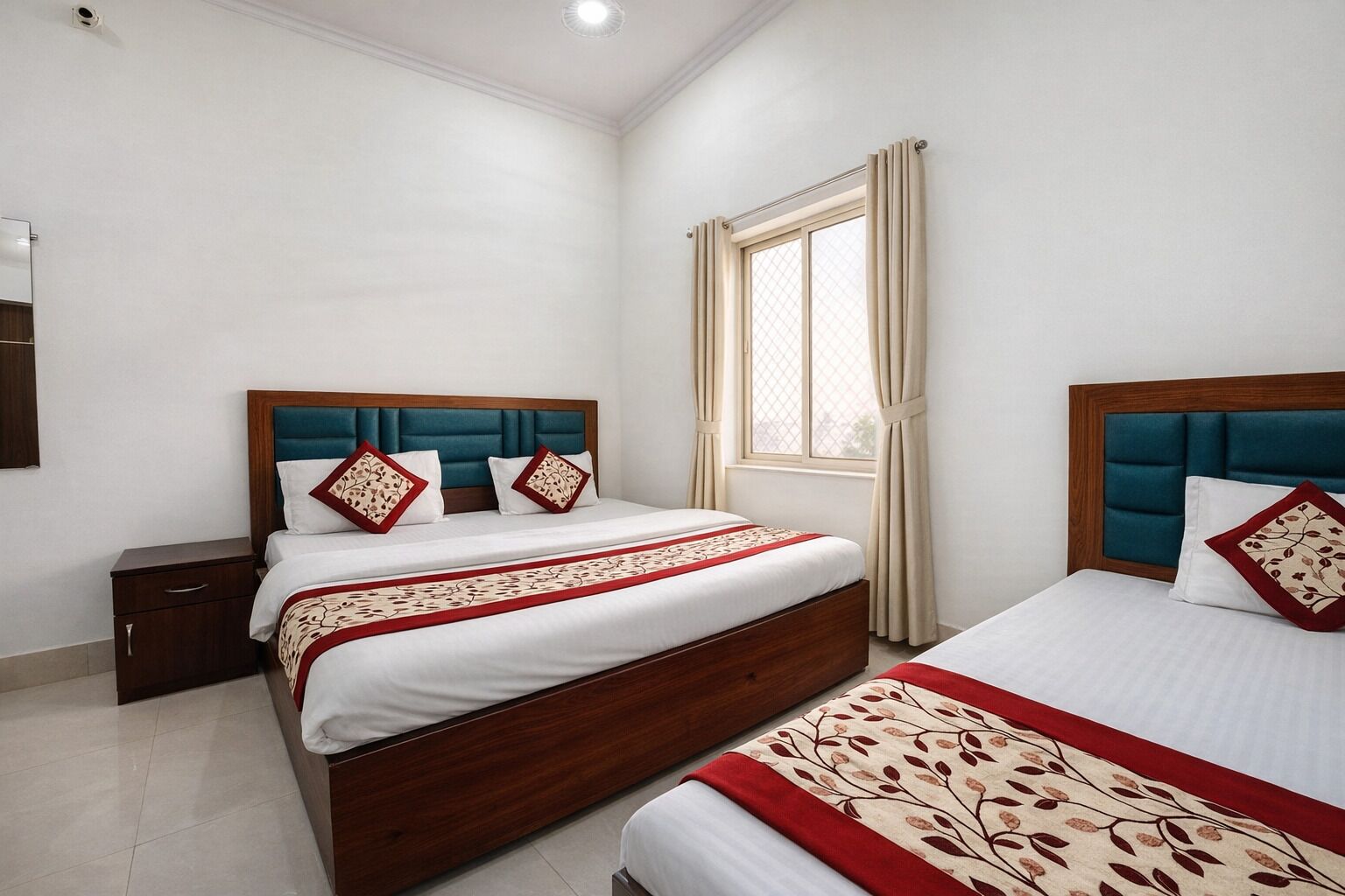 Quarto de hotel com duas camas, uma mesa de cabeceira, uma janela com cortinas e uma luminária no teto.