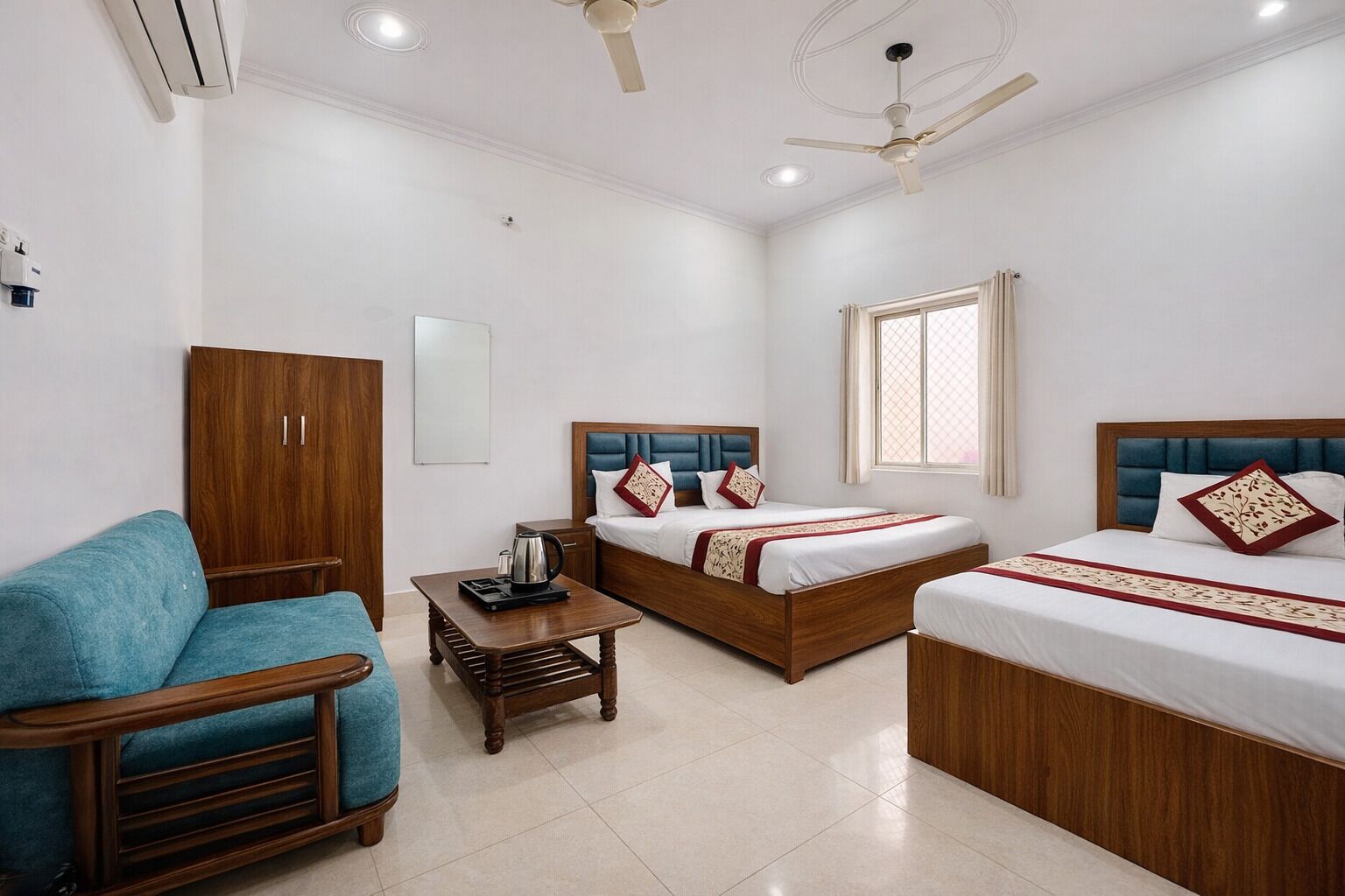 A hotel room with two beds, a sofa, a wooden cabinet, a coffee table, and a ceiling fan.
