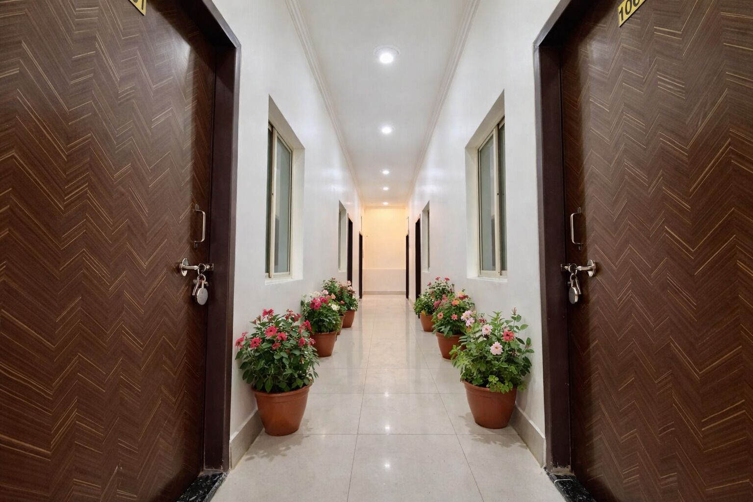 A hotel hallway with wooden doors, potted plants, and a tiled floor.