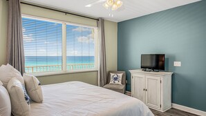 A bedroom with a bed, a television on a cabinet, and a view of the ocean through the window.