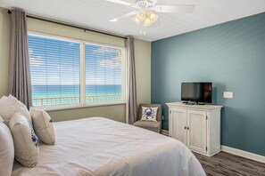 A bedroom with a bed, a television on a cabinet, and a view of the ocean through the window.