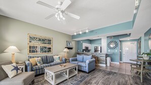 A living room with a ceiling fan, two sofas, a coffee table, and a kitchen area with a microwave.