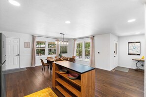A modern kitchen with a wooden island, dining area, and large windows.