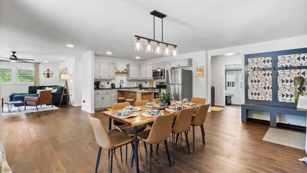 A modern kitchen with white cabinets, a central island, and a dining area with a wooden table and chairs. - The Pedaler's Choice,  Minutes to MTB Trails (Bella Vista)