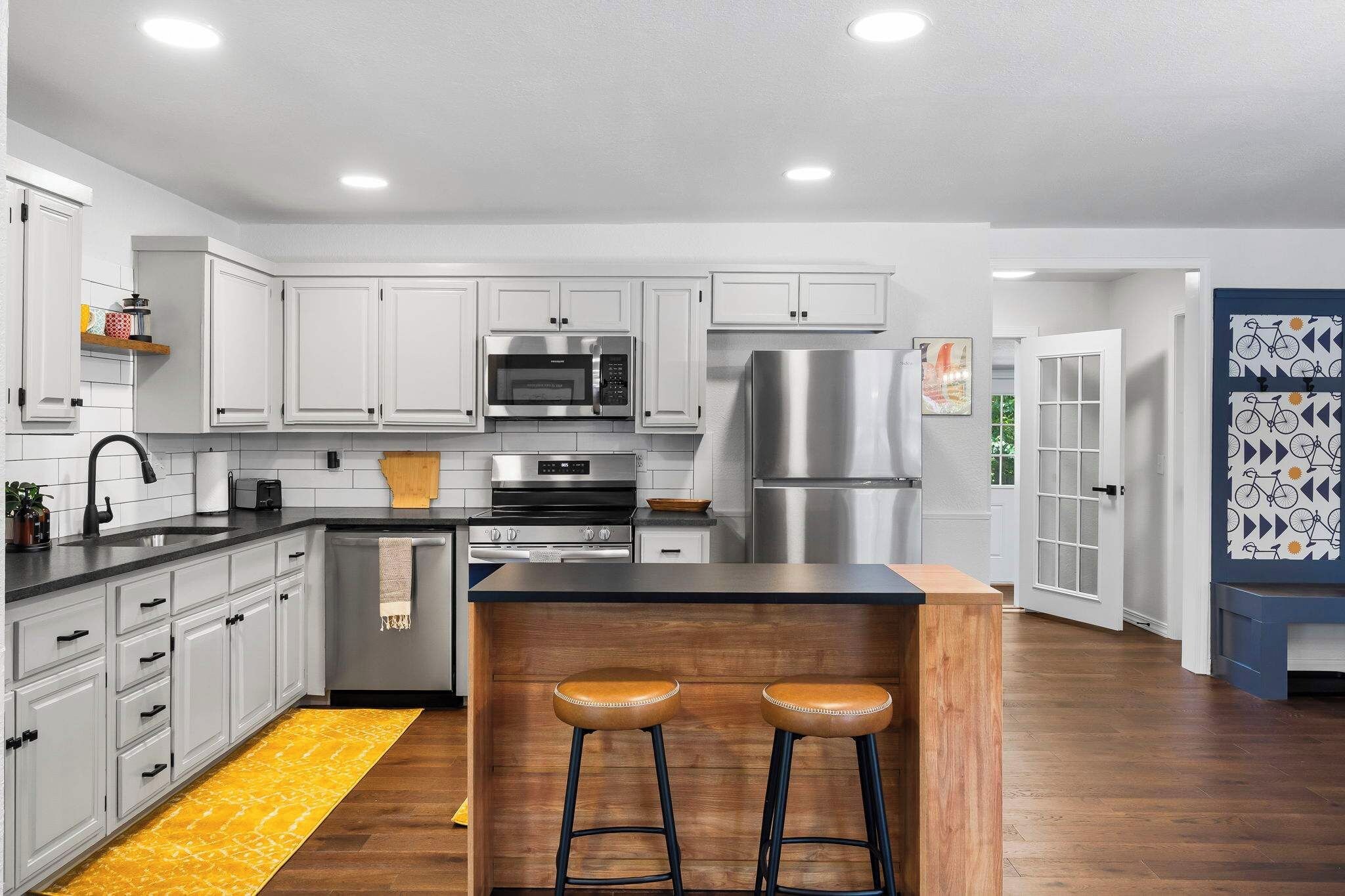 A modern kitchen with white cabinets, stainless steel appliances, and a wooden island with stools.