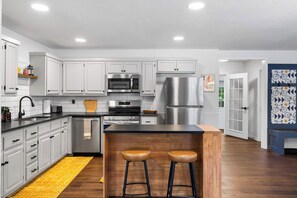Una cocina moderna con armarios blancos, electrodomésticos de acero inoxidable y una isla de madera con taburetes.