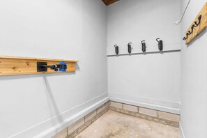 Una esquina de una habitación con un estante de madera, un enchufe en la pared y varios ganchos.