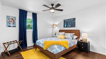 Un dormitorio con cama, mesita de noche, ventilador de techo, ventana con cortinas y un mapa en la pared.