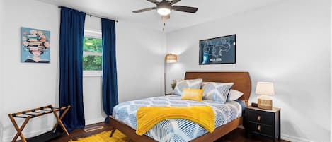 Ein Schlafzimmer mit Bett, Nachttisch, Deckenventilator, einem Fenster mit Vorhängen und einer Karte an der Wand.