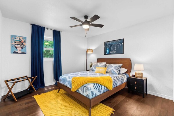 A bedroom with a bed, a nightstand, a ceiling fan, a window with curtains, and a map on the wall.