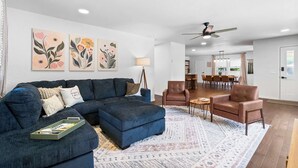 A modern living room with a sectional sofa, a coffee table, and a patterned rug. There are two armchairs and a dining area in the background. - The Pedaler's Choice,  Minutes to MTB Trails (Bella Vista)