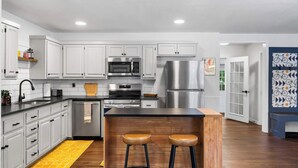 A modern kitchen with white cabinets, stainless steel appliances, and a wooden island with stools. - The Pedaler's Choice,  Minutes to MTB Trails (Bella Vista)